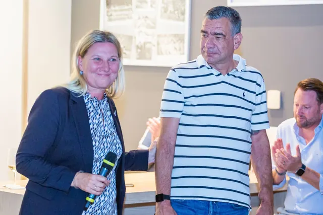 Eine Frau mit Mikrofon legt einem sichtlich bewegten Mann im gestreiften Poloshirt die Hand auf den Arm, rechts applaudiert ein Mann